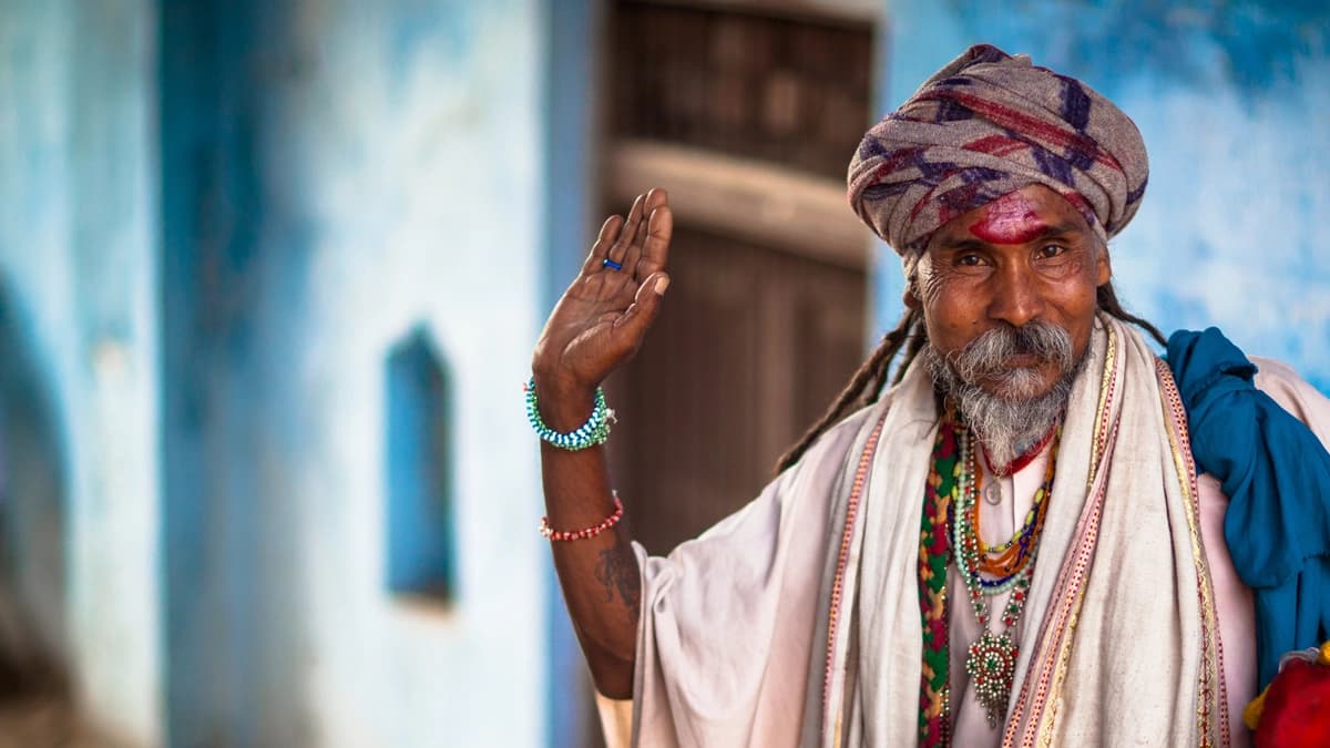 Photograph of man wearing a turban and waving his hand at the camera.