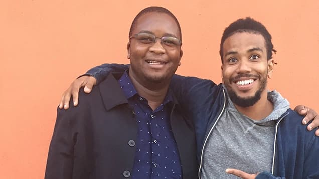Picture of two men with an arm around each other's shoulders, smiling at camera.