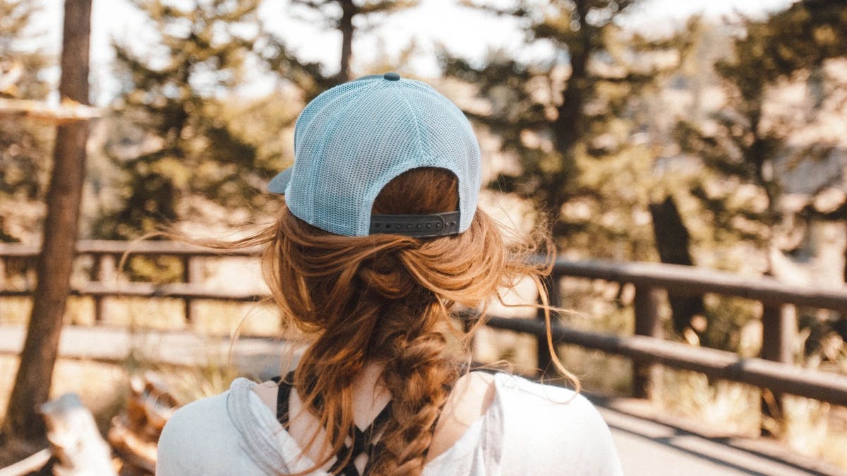Photo from behind a girl with a blue hat looking out towards a fence and trees
