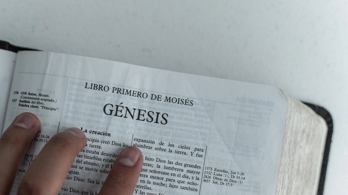 hands on the bible, open to the book of Genesis written in Spanish