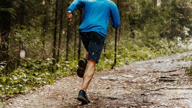 Man in blue shirt running on a trail in the woods during a rain