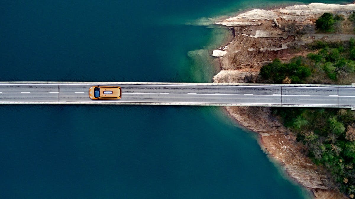 aerial view of car driving on bridge away from land