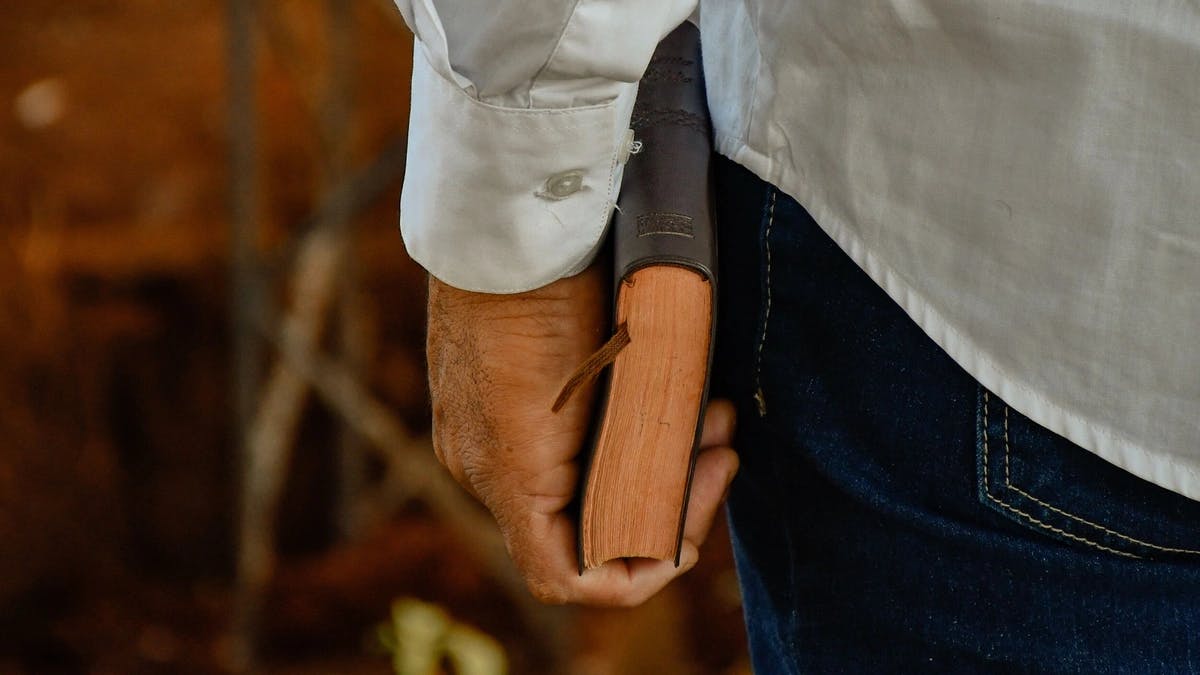 close up photo of pastors left hand at his side holding a bible