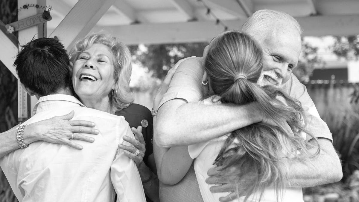 Older couple embraces their son and daughter in this black and white photo under a covering