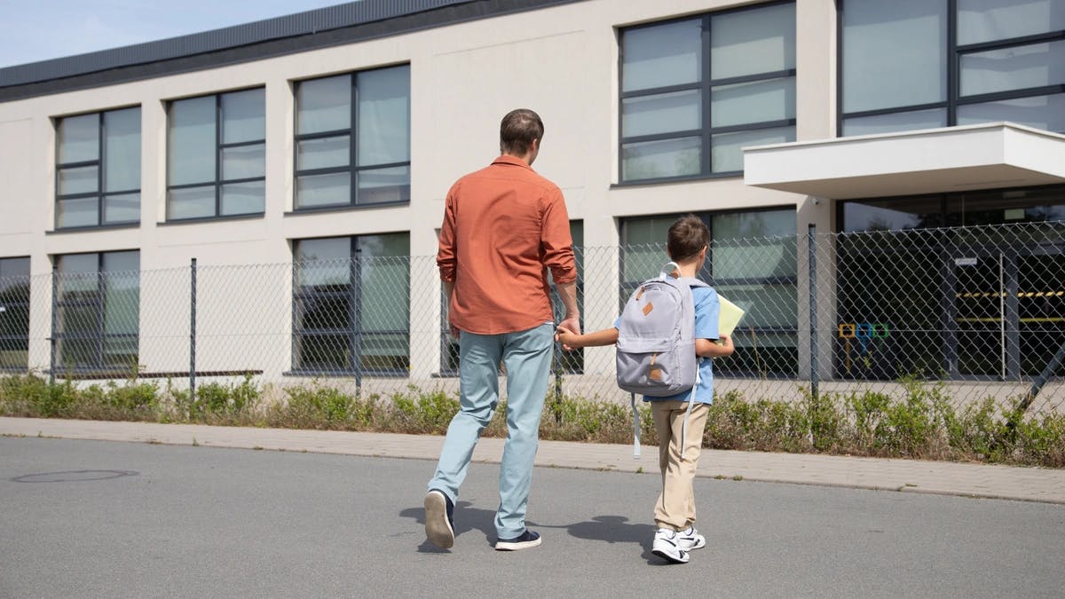 Dad holds his young son's hand as he walks him into the school building. 